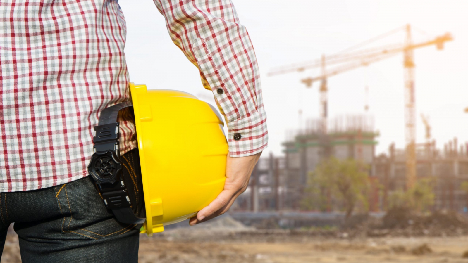 Hand's engineer worker holding yellow safety helmet with building on site background.