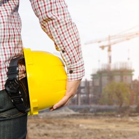 Hand's engineer worker holding yellow safety helmet with building on site background.